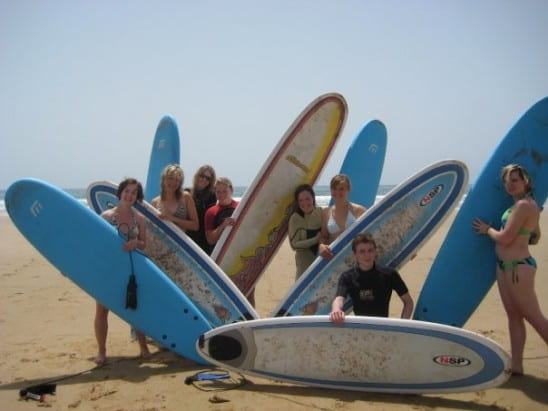 A group of people posing on a sandy beach with surfboards.